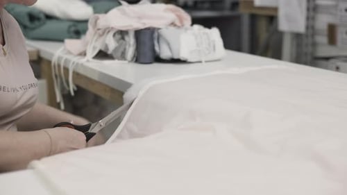 A Woman is Cutting Fabric in a Textile Workshop Using Scissors for Crafting and Sewing Purposes