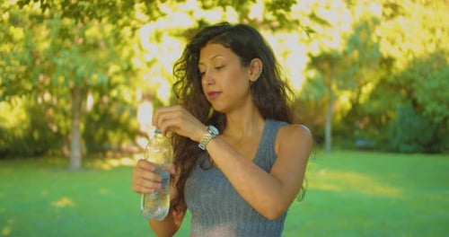 Pretty Young Female Drinking Water From Bottle in Tree Shade on Hot Summer Day