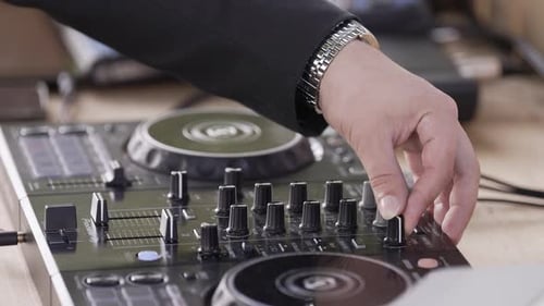 DJ's hand adjusting knobs and mixing tracks on a professional DJ console during a live performance