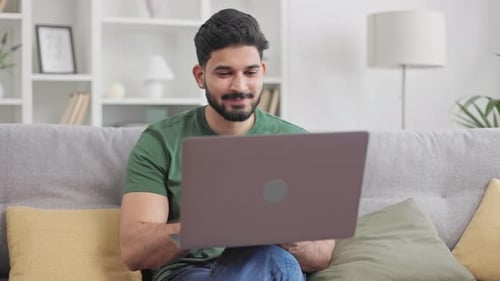Smiling Man Using Laptop on Couch