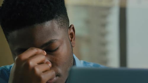 Young Adult Man Rubs Eye at Office Workplace