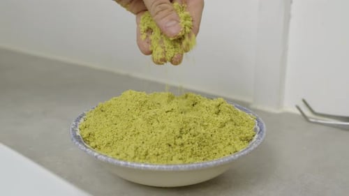 Chef puts hand into the plate with chopped nuts. Slow motion.