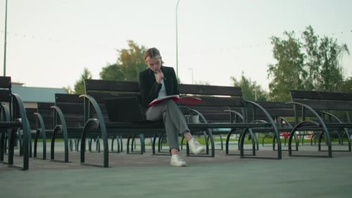 Focused Student Reading Book on Urban Bench with Laptop and Coffee in Quiet Park