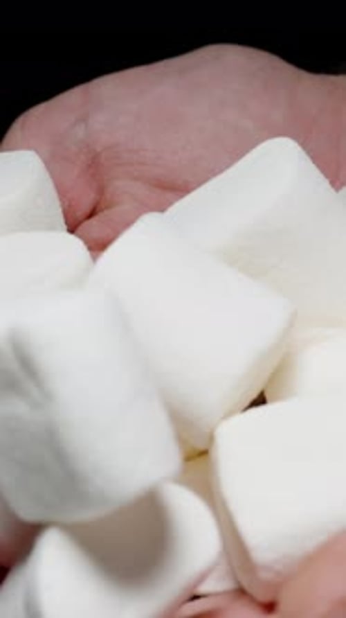 Vertical video. Man Slowly Pouring Many White Marshmallows from His Hands. Concept of Unhealthy