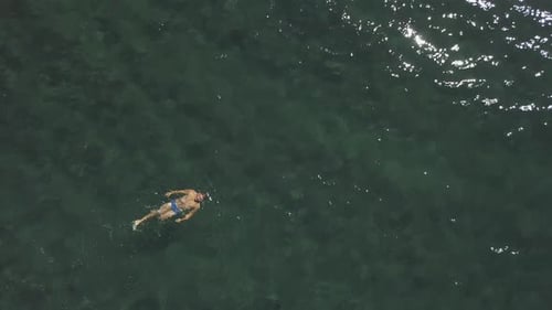 Circling Drone View A Young Masculine Man Floating and Swimming in Clear Water