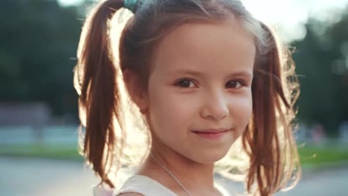 Pretty Caucasian Kid with Brown Eyes Looking Directly at Camera Smiling Park with Green Trees in