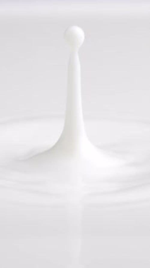 Goutte de lait frais qui tombe et éclabousse dans une mare laiteuse depuis le haut (anneaux au ralenti et sommet ondulé)