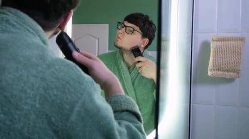 Man Trims Beard with Electric Razor in Mirror