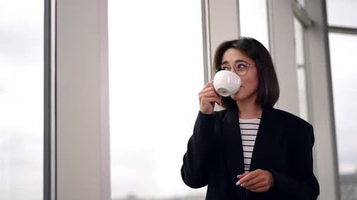 Woman Drinks Coffee near Office Building Window