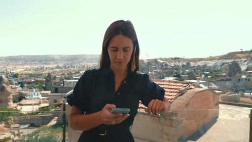 Young Female Tourist Working Remote on Smartphone on Vacation and Looking Around Beautiful View