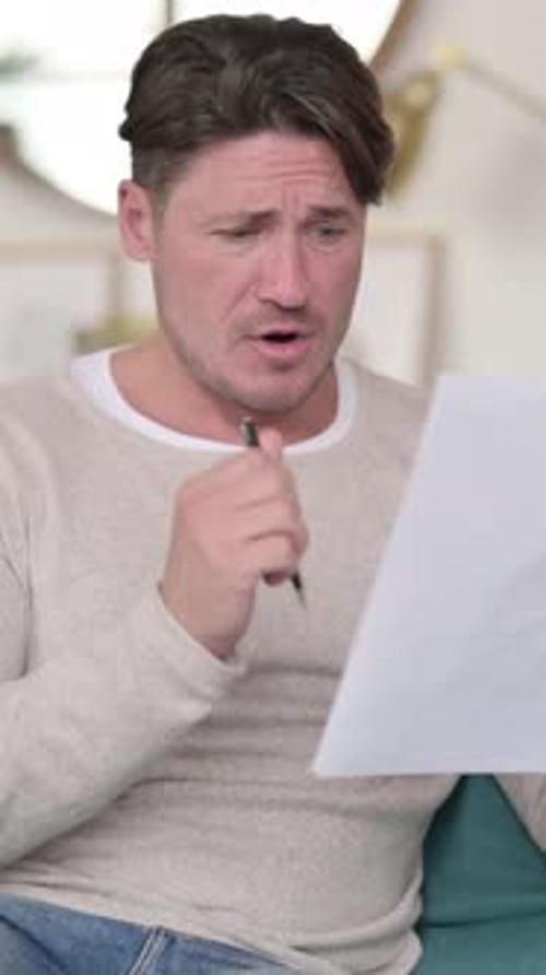 Man Sitting Indoors Looking at a Paper with Surprise