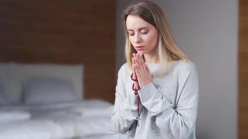 Woman Praying with Rosary Beads in Bedroom