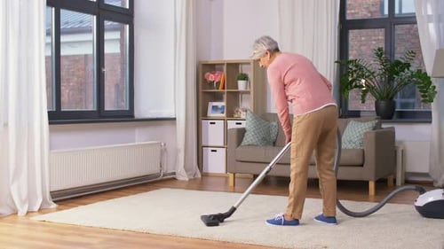 Senior woman vacuuming a light carpet in living room