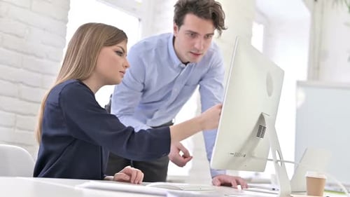 Woman Typing at Computer with Man Giving Feedback