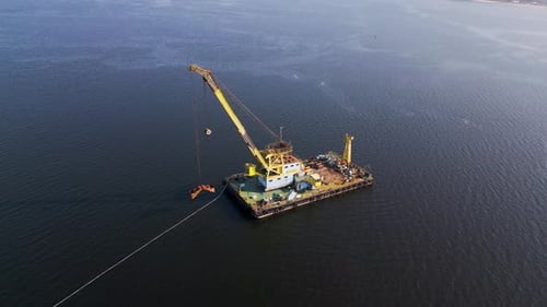 A Floating Crane Barge with a Large Yellow Crane Operates on Calm Waters Lifting an Object with Its