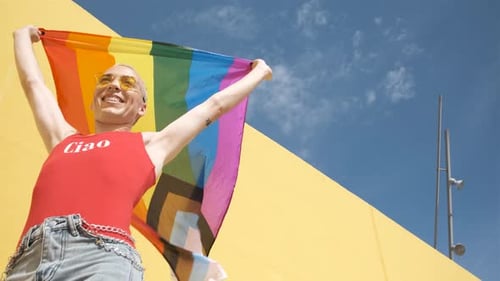 Person Holding Pride Flag Against Yellow Wall