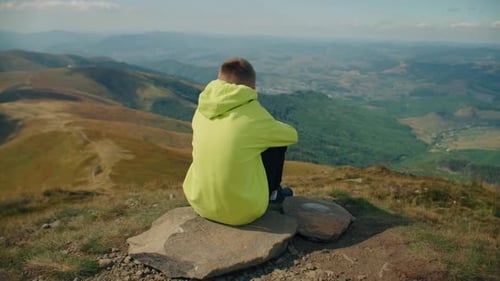 Jeune homme assis sur une pierre et observant le paysage
