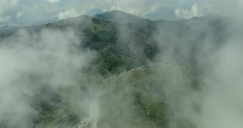 Flying trough white fluffy clouds above green mountain peaks. Beautiful summer sunny day on the high