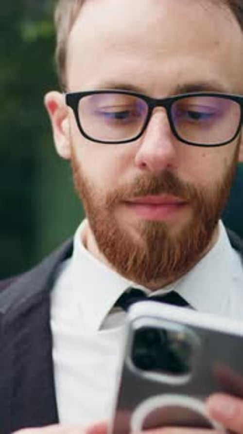 Close Up Cheerful Man in Glasses Sitting on Bench Outdoors Using Typing Smartphone Confident Bearded