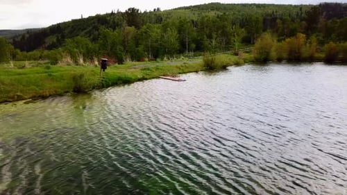 A drone shot over looking a pond with green meadow in view. (slow motion)
