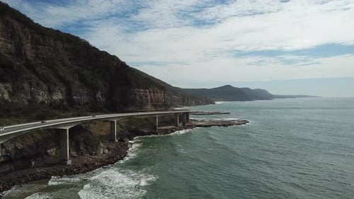 Luftbild: Drohne folgt Fahrzeugen, die über eine große Brücke entlang einer wunderschönen Küste fahren, in New S