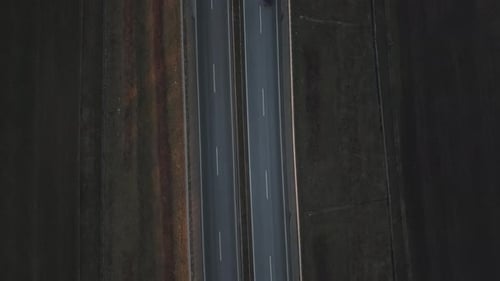 Top-down aerial view of a highway cutting through a rural landscape with a few cars traveling in