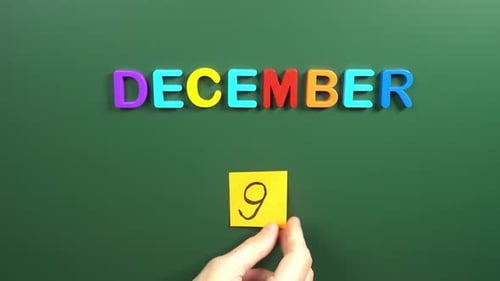 Hand sticking a sticker 9 December calendar day on school board. 9 date of December. Ninth day