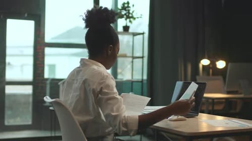 Attractive African American Woman Sitting on Chair Use Laptop Work with Paper in Office Serious