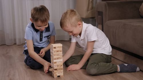 Two Little Boys are Playing an Educational Jenga Game at Home on the Floor
