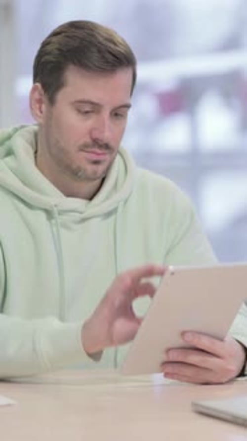 Man in Hoodie Using Digital Tablet at Table