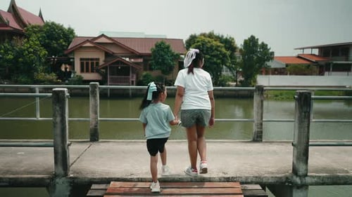 Mother and Daughter Holding Hands While Walking on a Bridge Over a River in Thailand