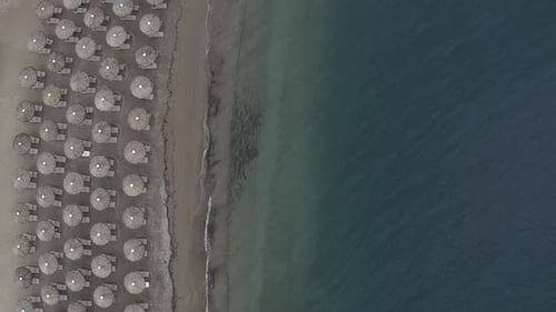 Flat lighting aerial descends toward beach umbrellas on sand beach