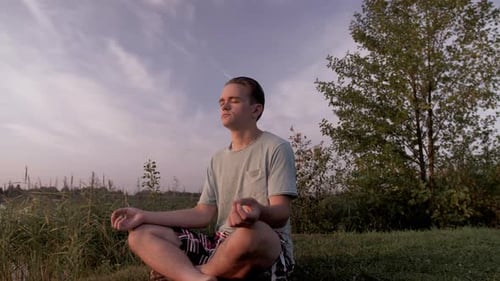 Man Meditating Outdoors Near Lake at Sunset