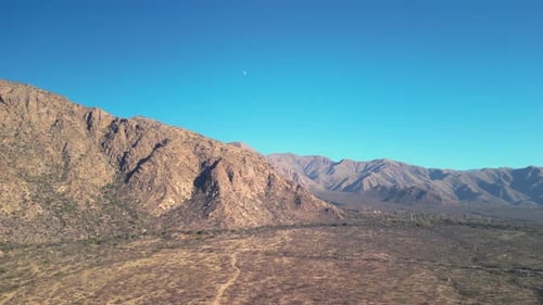 Aerial view drone flying over scenic rocky mountains with a clear blue sky.