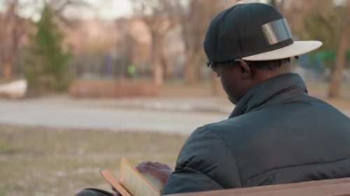 Man Reading Book On Park Bench Outdoors