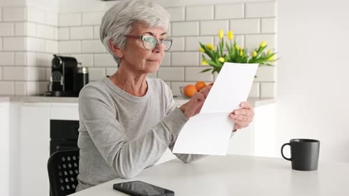 Senior Woman Reading Paper at Kitchen Table