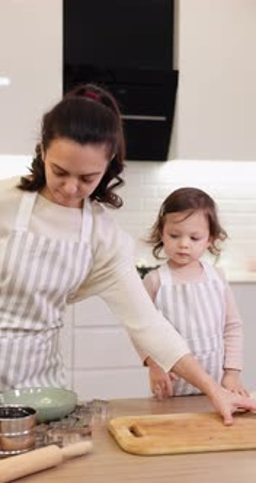 Mother and Her Little Child Daughter in Aprons Preparing the Dough in the Kitchen
