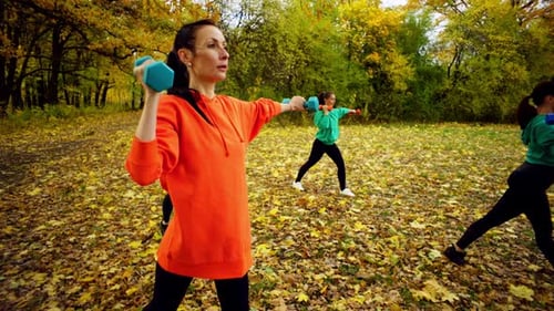 Women are Concentrating on Doing Sports with Dumbbells in the Autumn Park