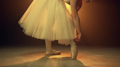 Ballerina tying her pointe shoes in golden light