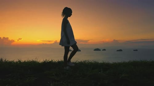 Woman Walking Green Hill Sunset Sky in Background