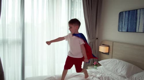 Young Boy Playing Superhero Jumping on Bed
