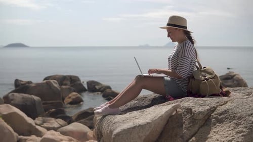 Young Woman Working on Laptop at Rocky Coastline