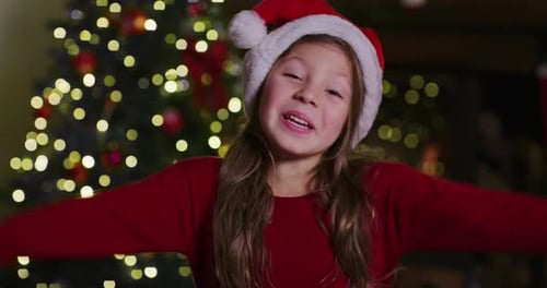 Joyful Girl Wearing Santa Hat in Front of Tree