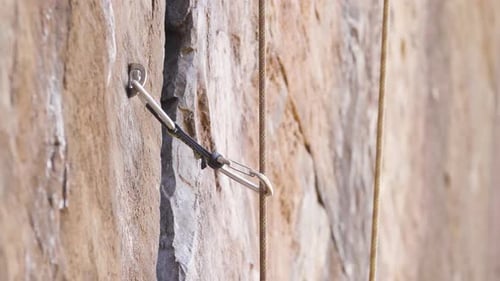 Nahaufnahme eines Karabiners, der an einem Haken an einer Felswand befestigt ist, mit einem Kletterseil, durch das ein Kletterseil gesteckt wird