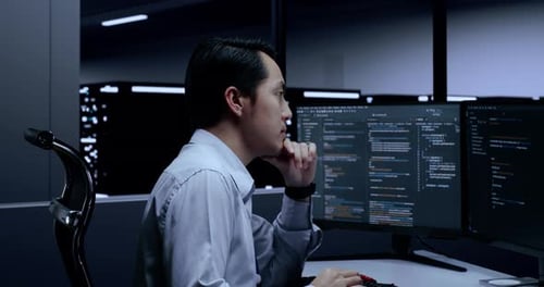 Male Programmer Thinking While Writing Code By Desktops Using Multiple Monitors In The Server Room