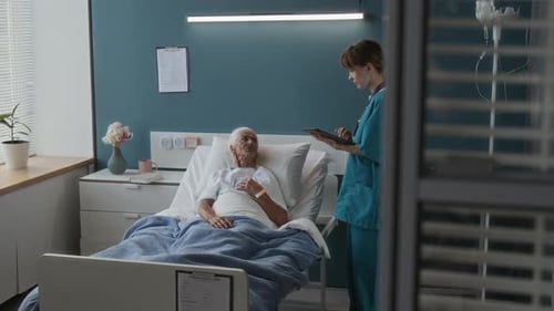 Medical Worker Holding Tablet Speaking with Senior Woman Lying in Hospital Bed