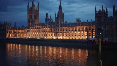 View of the Palace of Westminster at night with its lights reflecting on the River Thames, London, E