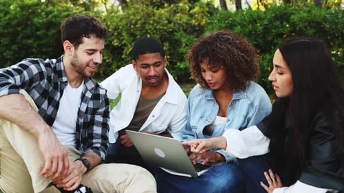 Diverse students working together on laptop in park