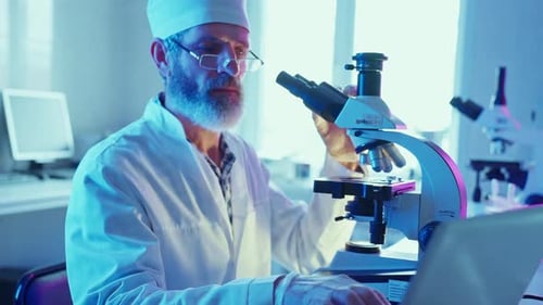 Scientist Uses Microscope and Laptop in Laboratory