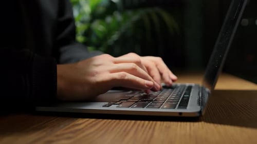 A man is programming, typing a code on a laptop at night in an institution, possibly a hacker